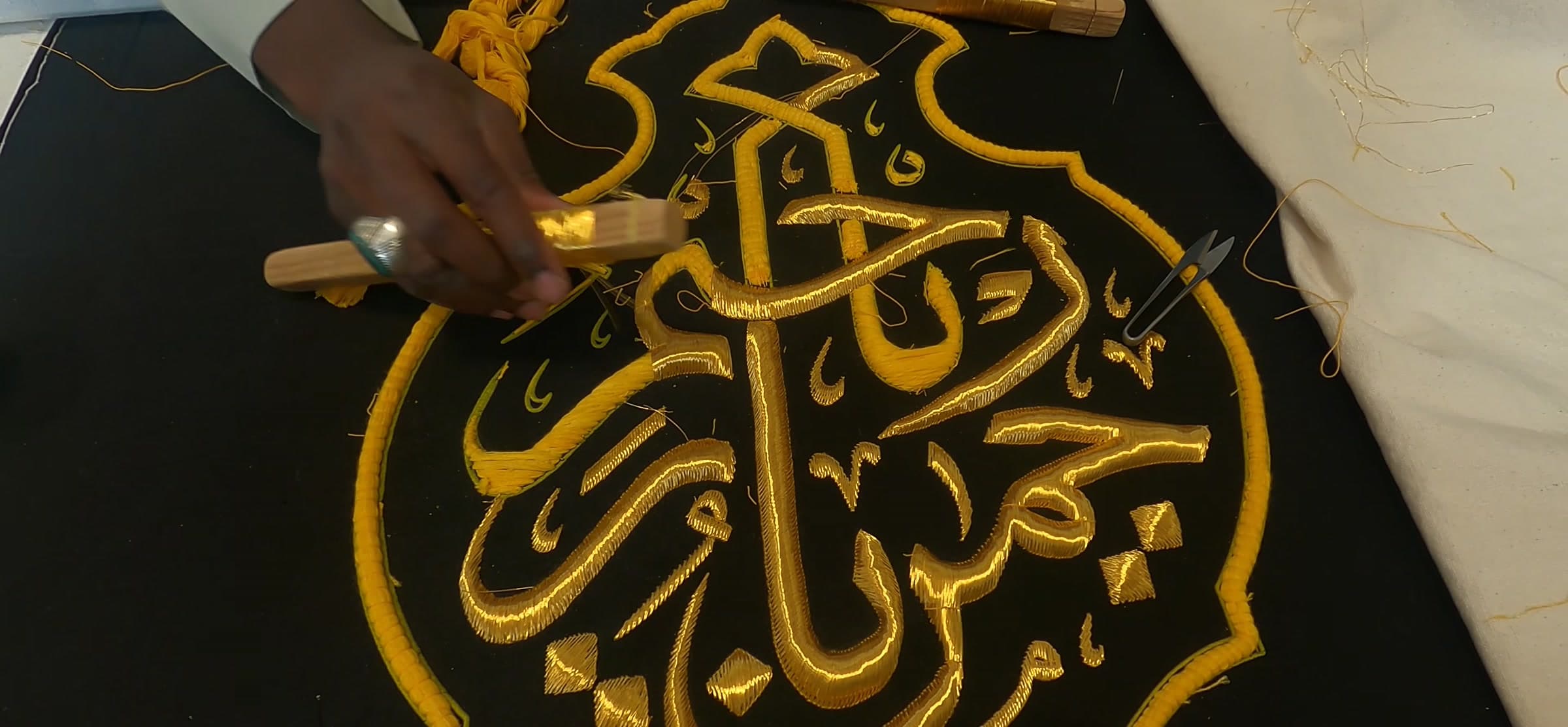 Gold thread calligraphy worked by hand onto black cloth.