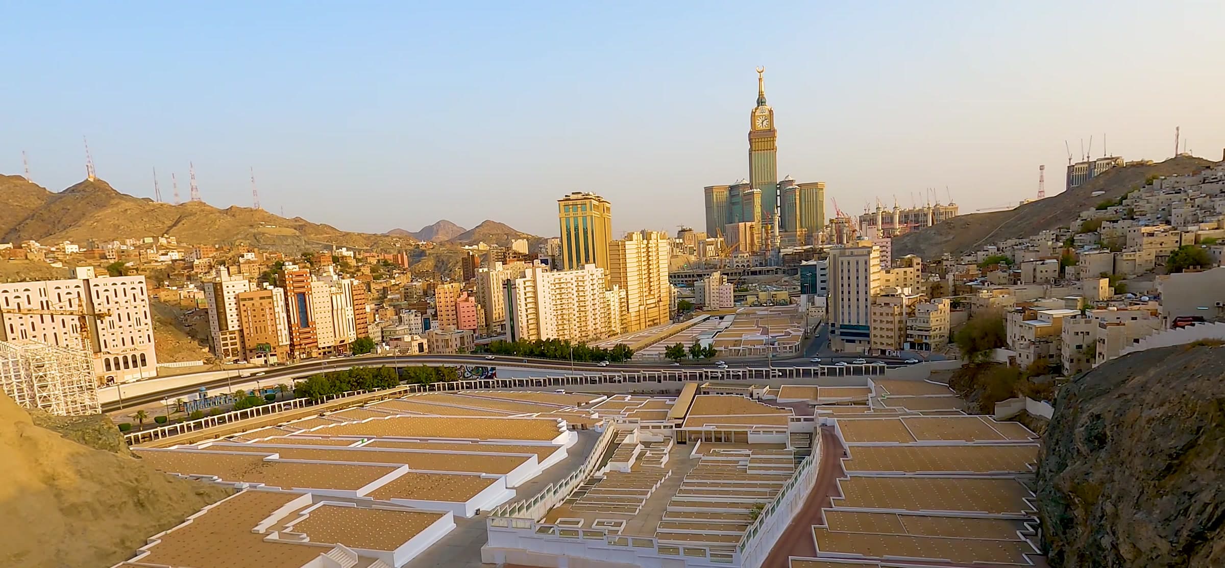The Makkah skyline at golden hour, hotel towers rising above the valley.
